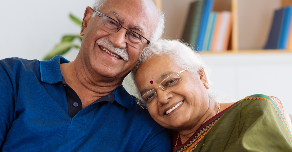 Elderly Indian Malaysian husband and wife couple smiling and sitting close to each other